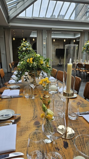 Banquette tablescape design at hampton manor for Mediterranean Shipping Company - Tall gold stands with large yellow and ivory flowers displays - short stone urns of flowers with gold and glass bud vases of flowers and gold and glass candle holders in between