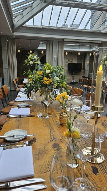 Banquette tablescape design at hampton manor for Mediterranean Shipping Company - Tall gold stands with large yellow and ivory flowers displays - short stone urns of flowers with gold and glass bud vases of flowers and gold and glass candle holders in between