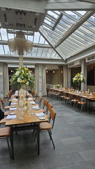 Banquette tablescape design at hampton manor for Mediterranean Shipping Company - Tall gold stands with large yellow and ivory flowers displays - short stone urns of flowers with gold and glass bud vases of flowers and gold and glass candle holders in between