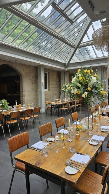 Banquette tablescape design at hampton manor for Mediterranean Shipping Company - Tall gold stands with large yellow and ivory flowers displays - short stone urns of flowers with gold and glass bud vases of flowers and gold and glass candle holders in between