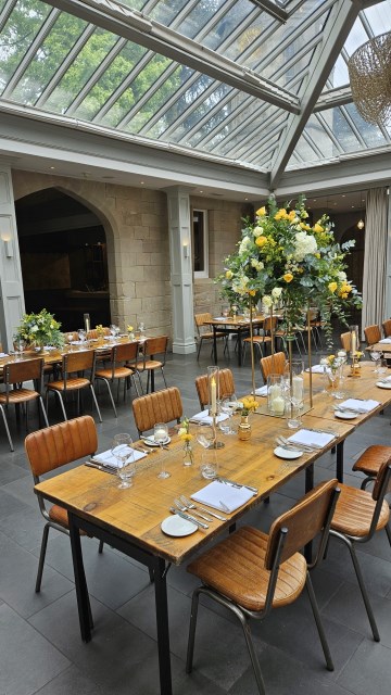 Banquette tablescape design at hampton manor for Mediterranean Shipping Company - Tall gold stands with large yellow and ivory flowers displays - short stone urns of flowers with gold and glass bud vases of flowers and gold and glass candle holders in between