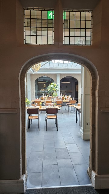 Banquette tablescape design at hampton manor for Mediterranean Shipping Company - Tall gold stands with large yellow and ivory flowers displays - short stone urns of flowers with gold and glass bud vases of flowers and gold and glass candle holders in between