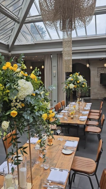 Banquette tablescape design at hampton manor for Mediterranean Shipping Company - Tall gold stands with large yellow and ivory flowers displays - short stone urns of flowers with gold and glass bud vases of flowers and gold and glass candle holders in between