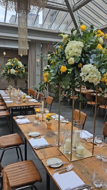 Banquette tablescape design at hampton manor for Mediterranean Shipping Company - Tall gold stands with large yellow and ivory flowers displays - short stone urns of flowers with gold and glass bud vases of flowers and gold and glass candle holders in between