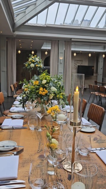 Banquette tablescape design at hampton manor for Mediterranean Shipping Company - Tall gold stands with large yellow and ivory flowers displays - short stone urns of flowers with gold and glass bud vases of flowers and gold and glass candle holders in between