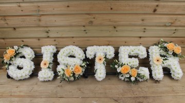 Sister funeral tribute foliage edge based in white chrysanthemum with peach rose sprays 