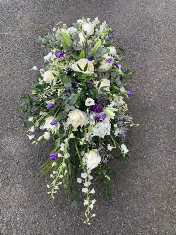 Casket spray in ivory and purple featuring Rose, Lily, Lisianthus,Delphiniums, Limonium with Eucalyptus and soft Ruscuss